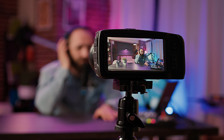 Selective focus on digital video camera screen recording male vlogger with headphones talking at microphone